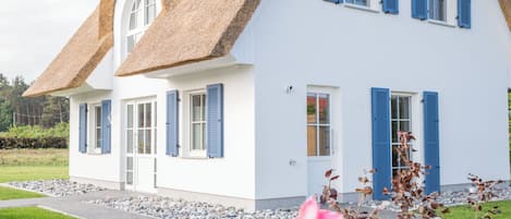 A white house with blue shutters and a thatched roof.