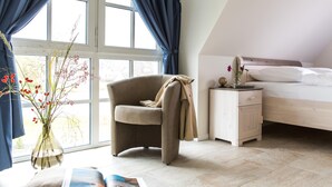 A bedroom with a bed, a nightstand, a chair, and a window with curtains. - Ferienhaus Schilfrohrsänger 31 - Der Natur Ganz nah (Fuhlendorf)