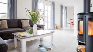 A modern living room with a sofa, coffee table, and a wood-burning stove. - Ferienhaus Schilfrohrsänger 31 - Der Natur Ganz nah (Fuhlendorf)