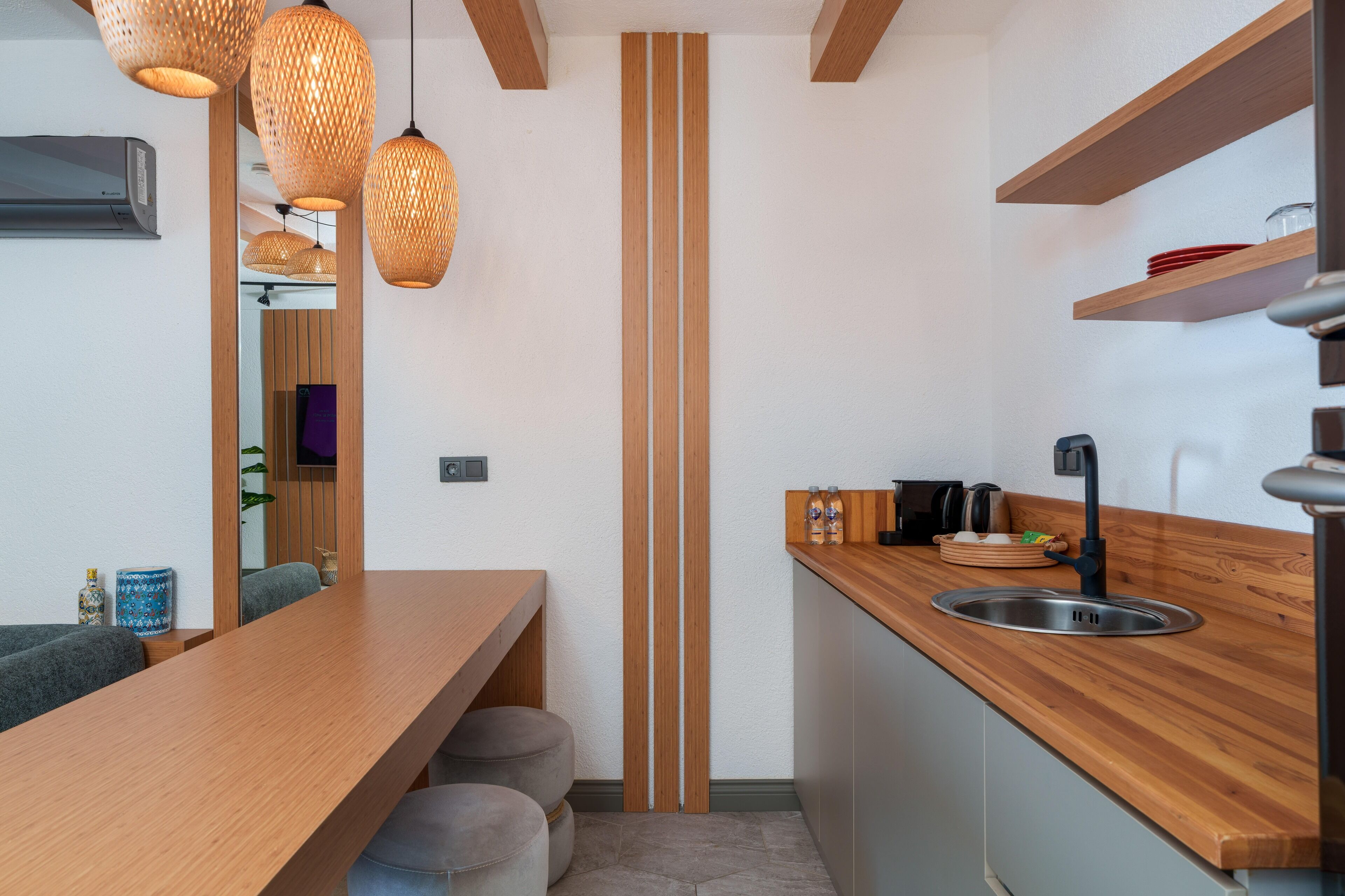 A modern kitchen with wooden countertops, a central vertical wooden accent, and hanging wicker pendant lights.