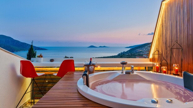 Un jacuzzi en una terraza de madera con vista al mar y un paisaje urbano al fondo.