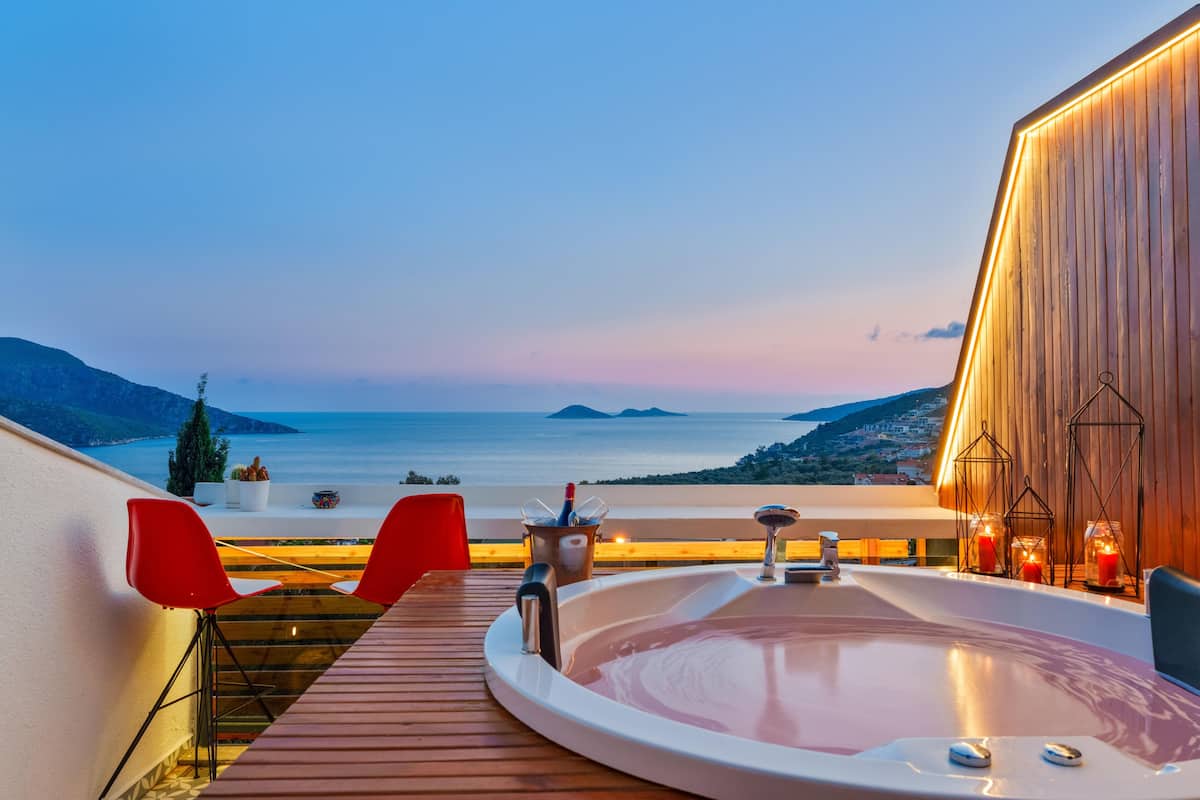 A hot tub on a wooden deck with a view of the sea and a cityscape in the background.