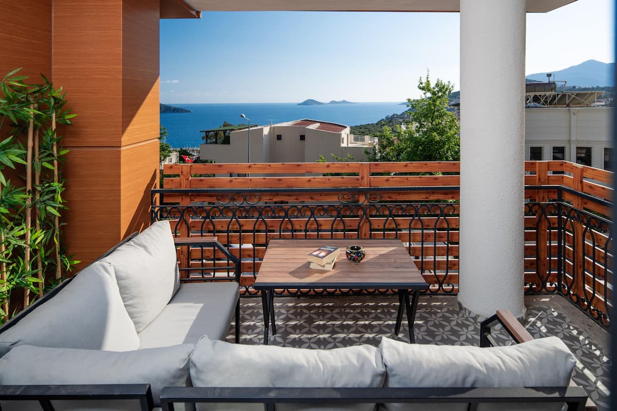 A balcony with a wooden table, a sofa, and a view of the sea.