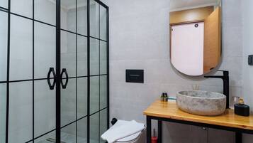 Un baño moderno con cabina de ducha de vidrio, un mueble de tocador de madera con lavabo redondo y un espejo sobre el lavabo.