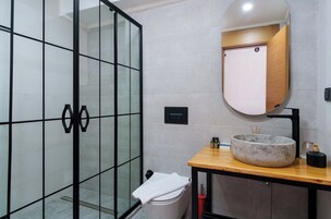 Un baño moderno con cabina de ducha de vidrio, un mueble de tocador de madera con lavabo redondo y un espejo sobre el lavabo.