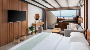 Un hotel moderno con una cama grande, un televisor de pantalla plana, un panel de pared de madera, un escritorio con espejo y vistas al mar.