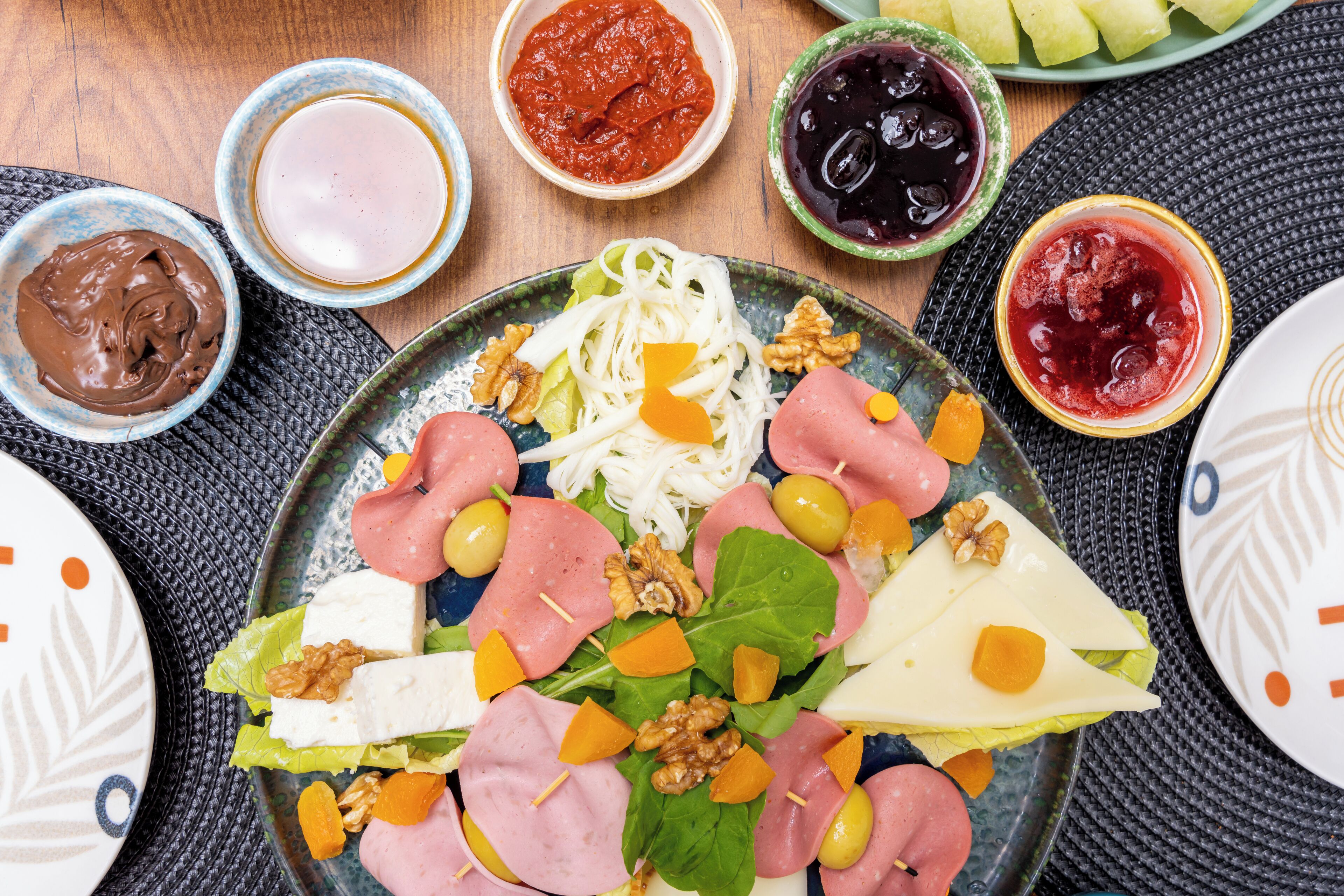 A plate of assorted meats, cheeses, and vegetables with various condiments in the background.