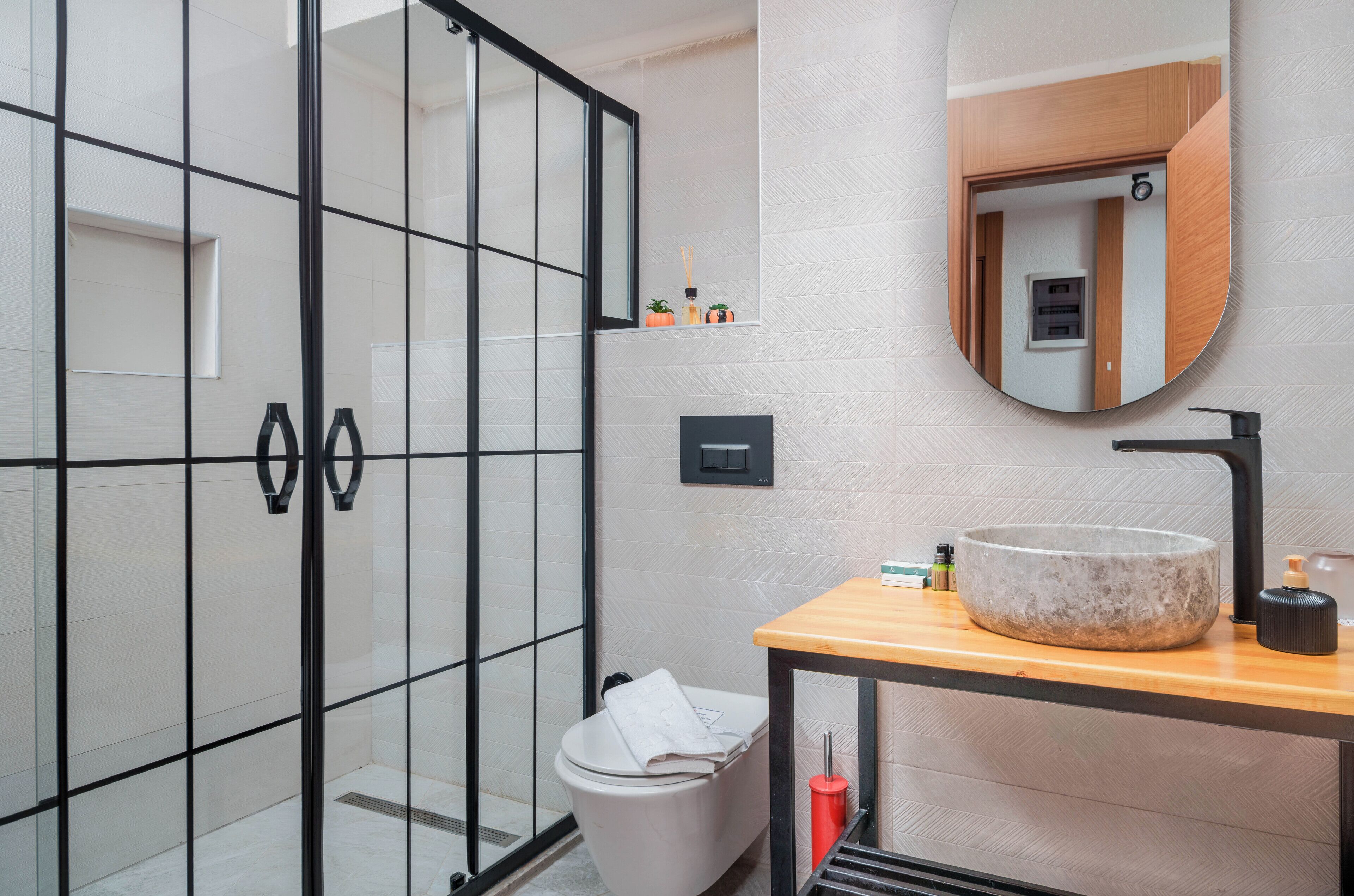 Un baño moderno con cabina de ducha de vidrio, tocador de madera con lavamanos de piedra y espejo con marco de madera.
