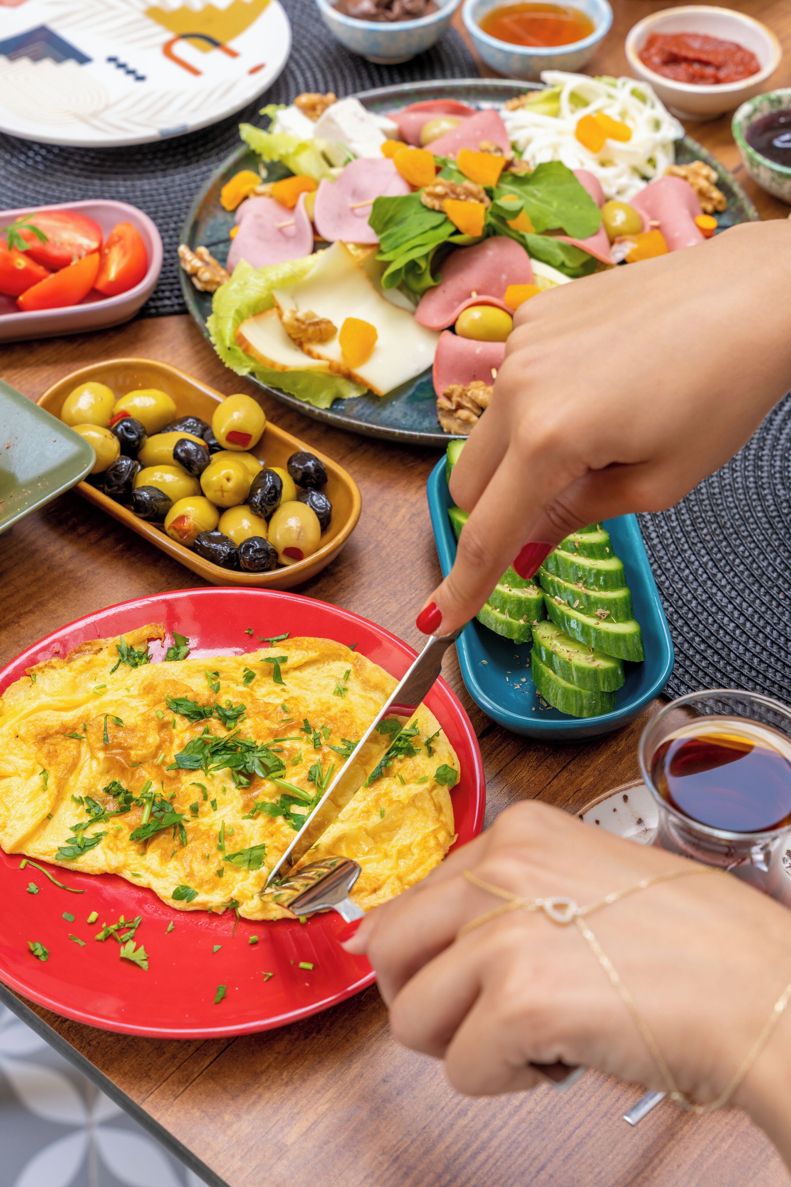 Une table sur laquelle on trouve différents plats, notamment une assiette rouge contenant des œufs brouillés, une assiette bleue avec des tranches de concombre et une assiette avec une salade.