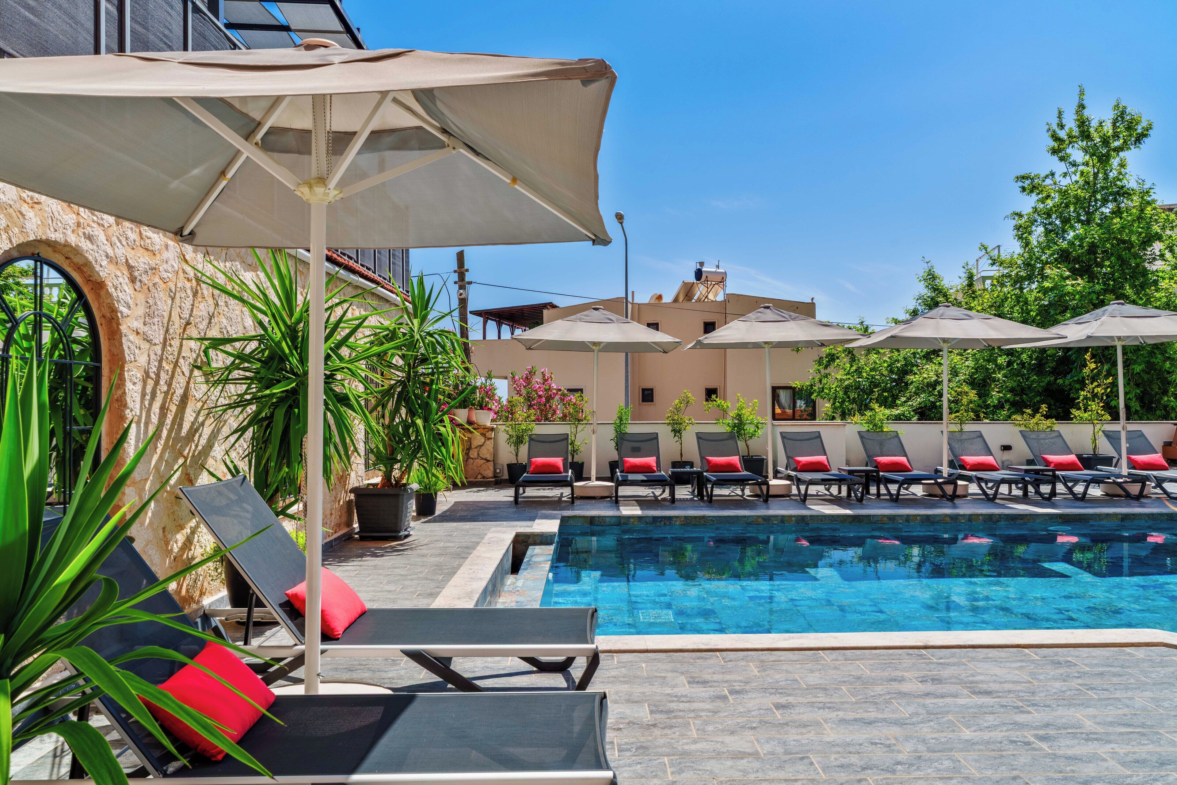 A swimming pool with lounge chairs and umbrellas, surrounded by greenery and a stone wall.