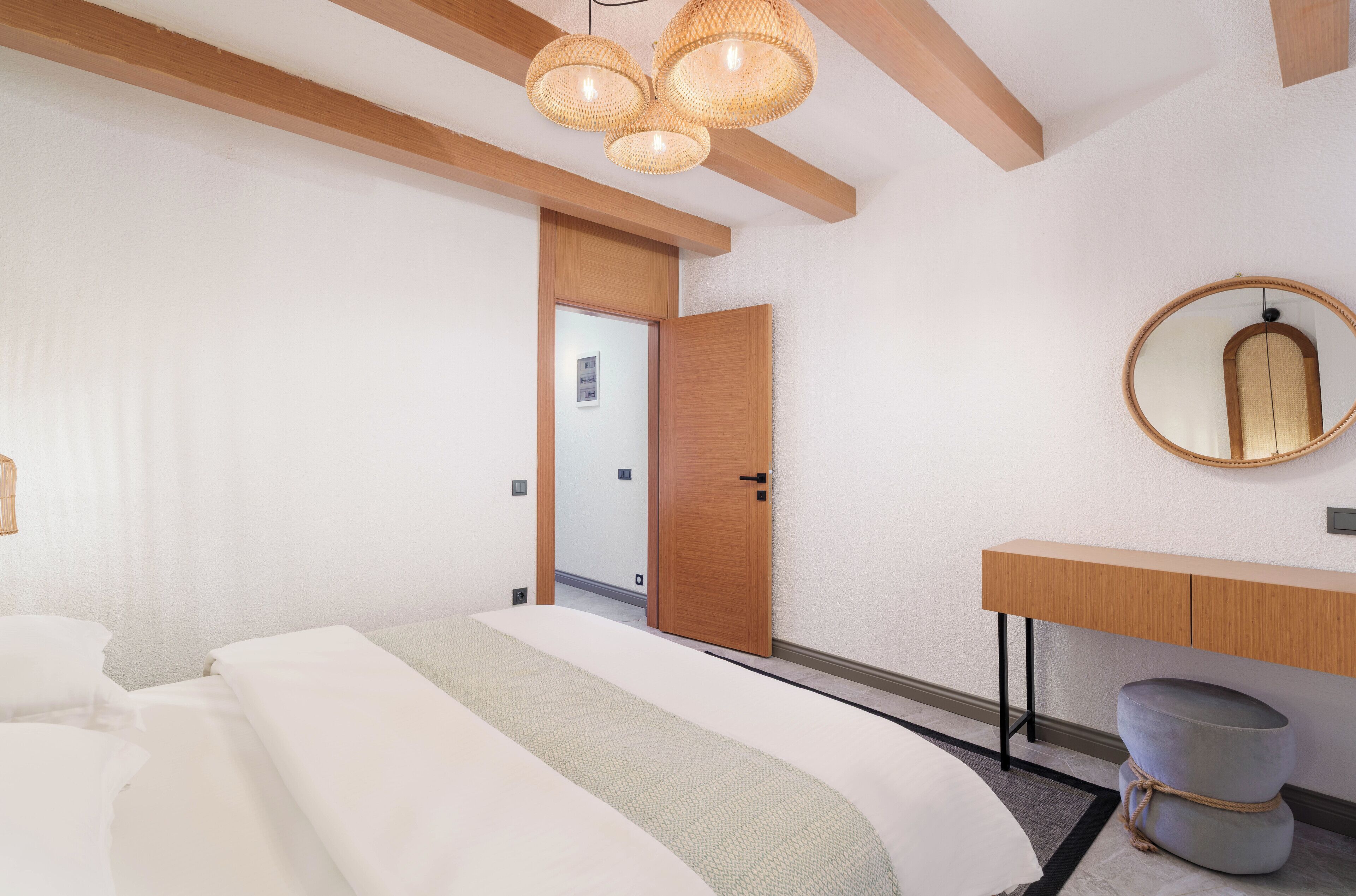 A modern hotel room with a large bed, wooden ceiling beams, a round mirror, and a wooden console table.