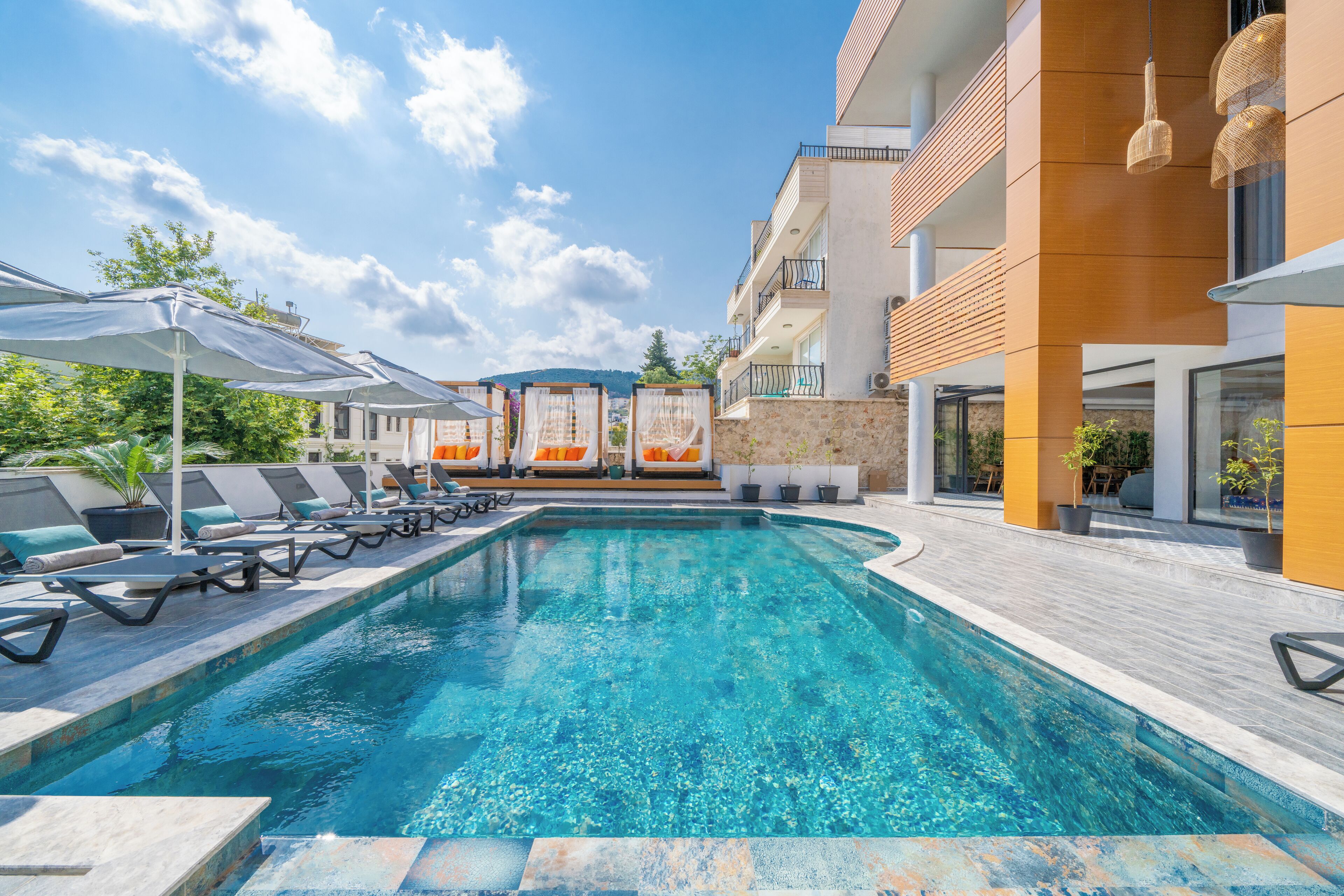 A modern pool area with lounge chairs and umbrellas, a clear blue pool, and a building with balconies and large windows.