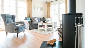 Een gezellige woonkamer met een bank, fauteuil en een zwarte houtkachel.
