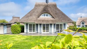 Een rieten huis met een groot raam en een verzorgd gazon.