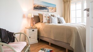 Een slaapkamer met een bed, nachtkastje, lamp, stoel en raam met gordijnen.