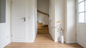 Een hal met een houten trap, witte muren en een witte deur.