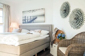 A bedroom with a bed, a nightstand, a lamp, a wicker chair, and wall decorations.