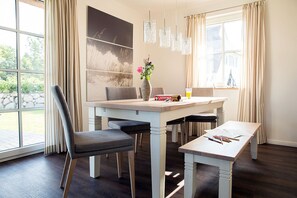 A dining area with a table, chairs, a vase with flowers, a game, and a window with curtains.