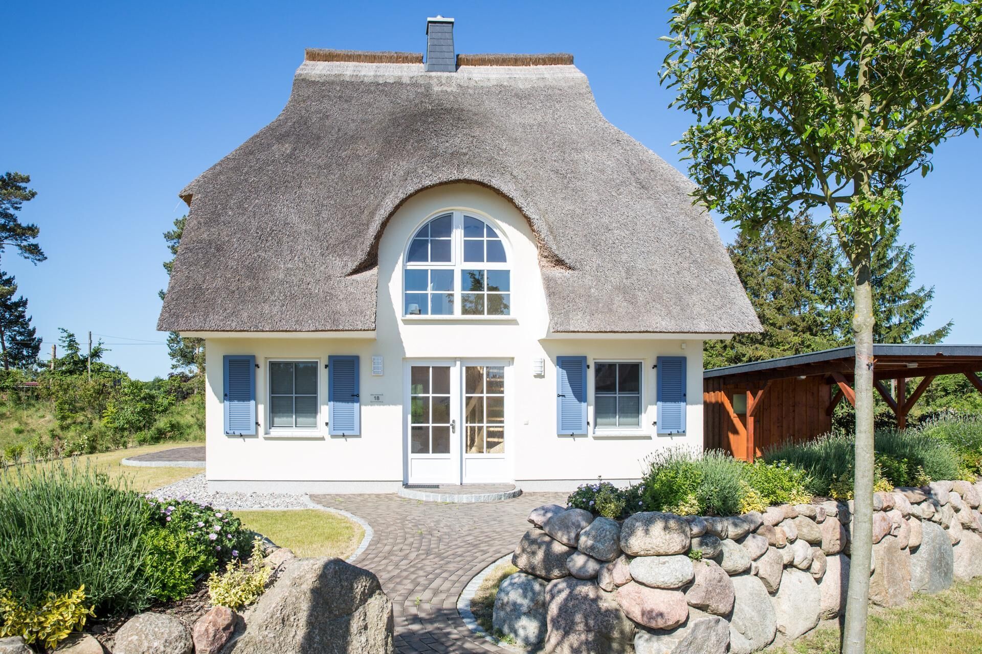 Ein Haus mit Strohdach, weißen Wänden und blauen Fensterläden.