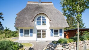A house with a thatched roof, white walls, and blue shutters. - Ferienhaus Schilfrohrsänger 48 - Der Natur Ganz nah (Fuhlendorf)