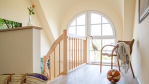 A spacious room with a wooden floor, a basketball, a wicker chair, and a large window. - Ferienhaus Schilfrohrsänger 48 - Der Natur Ganz nah (Fuhlendorf)