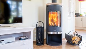 A modern living room with a wood-burning stove, a TV, and a fireplace. - Ferienhaus Schilfrohrsänger 48 - Der Natur Ganz nah (Fuhlendorf)