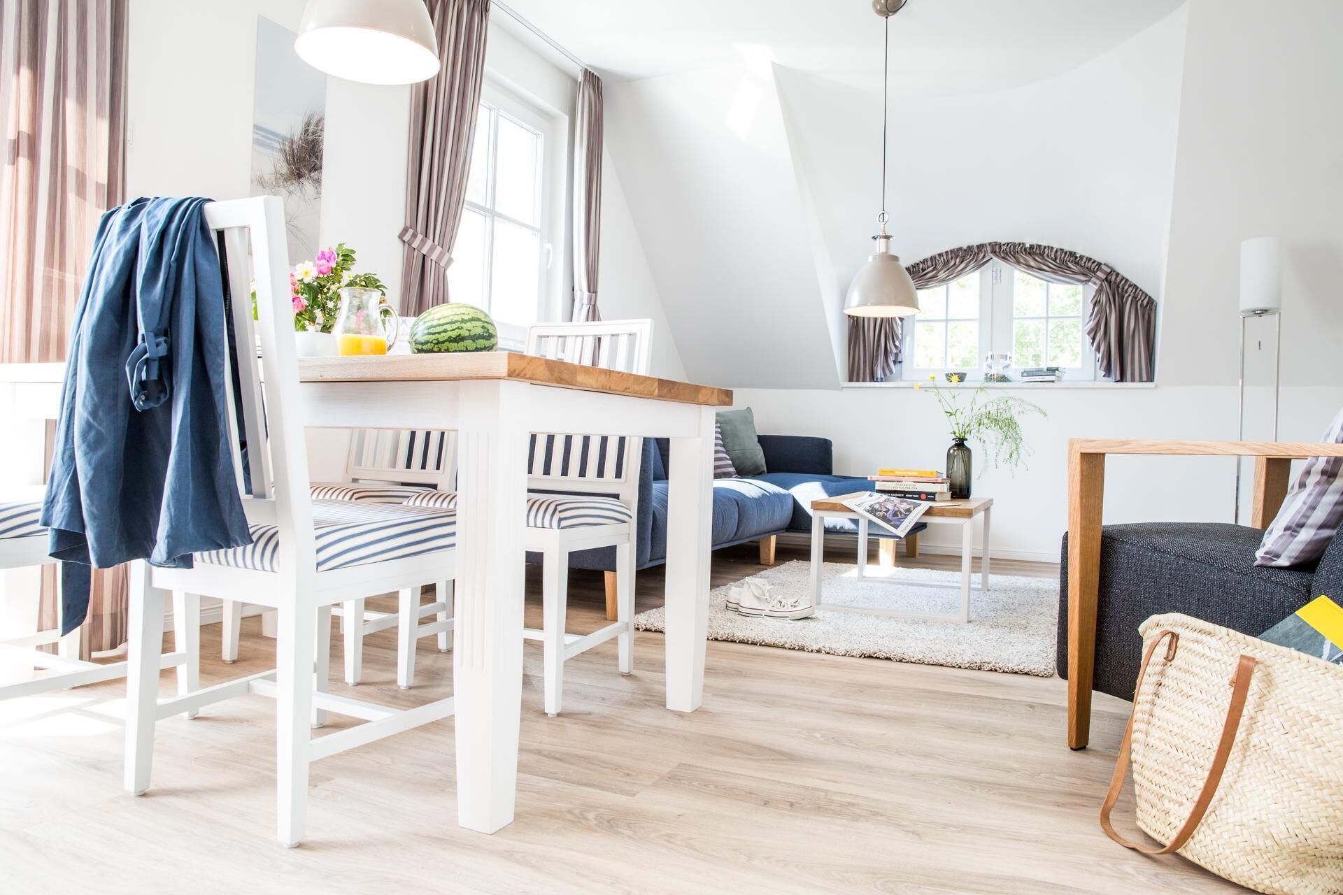 Un salon moderne avec un canapé blanc, des fauteuils à rayures, une table basse en bois et un coin repas comprenant une table et des chaises blanches.