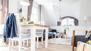 Una sala de estar moderna con un sofá blanco, sillas a rayas, una mesa de centro de madera y un comedor con mesa y sillas blancas.