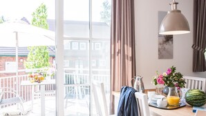 Cocina luminosa con un ventanal amplio, muebles blancos y una mesa lista para el desayuno, con sandía y jugo de naranja.