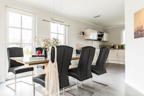 Une cuisine moderne avec des meubles blancs, un coin repas avec des chaises noires et une table en verre, et une grande fenêtre qui laisse entrer la lumière naturelle.