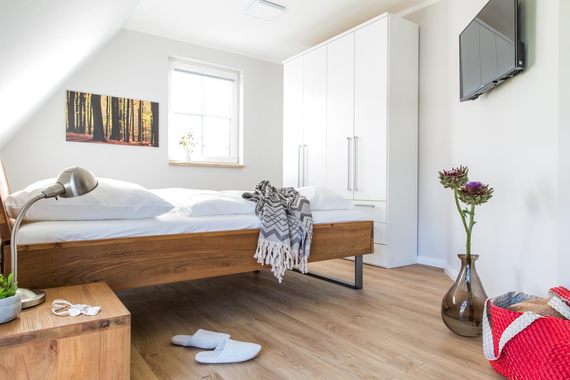 A bedroom with a bed, a desk, a chair, a TV, and a window.