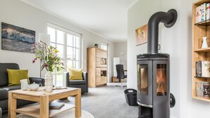 Een moderne woonkamer met een grote, zwarte houtkachel, een houten salontafel, een bank en een boekenkast.