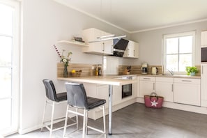 Une cuisine moderne avec des meubles blancs, un four encastré, une machine à café et un petit coin repas avec deux chaises.