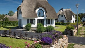 Een huis met rieten dak en witte muren, omgeven door een verzorgde tuin met lavendel en rozen.