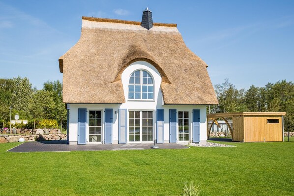 A house with a thatched roof, white walls, and blue shutters.