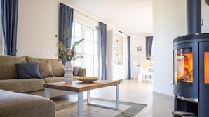 A modern living room with a sofa, a coffee table, a fireplace, and a bookshelf. - Ferienhaus Schilfrohrsänger 36 - Der Natur Ganz nah (Fuhlendorf)