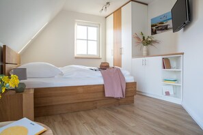 A bedroom with a wooden bed, a window, a TV mounted on the wall, and a bookshelf.