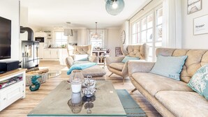 Een moderne woonkamer met een bank, salontafel en televisie. Achtergrond is een keuken met een eethoek.