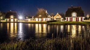 Een uitzicht op een meer met een rij traditionele huizen met rieten daken, verlicht door lantaarns.