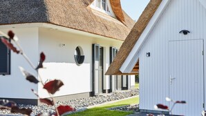 Ein Haus mit einem Strohdach, einer weißen Fassade und einem kleinen Schuppen.