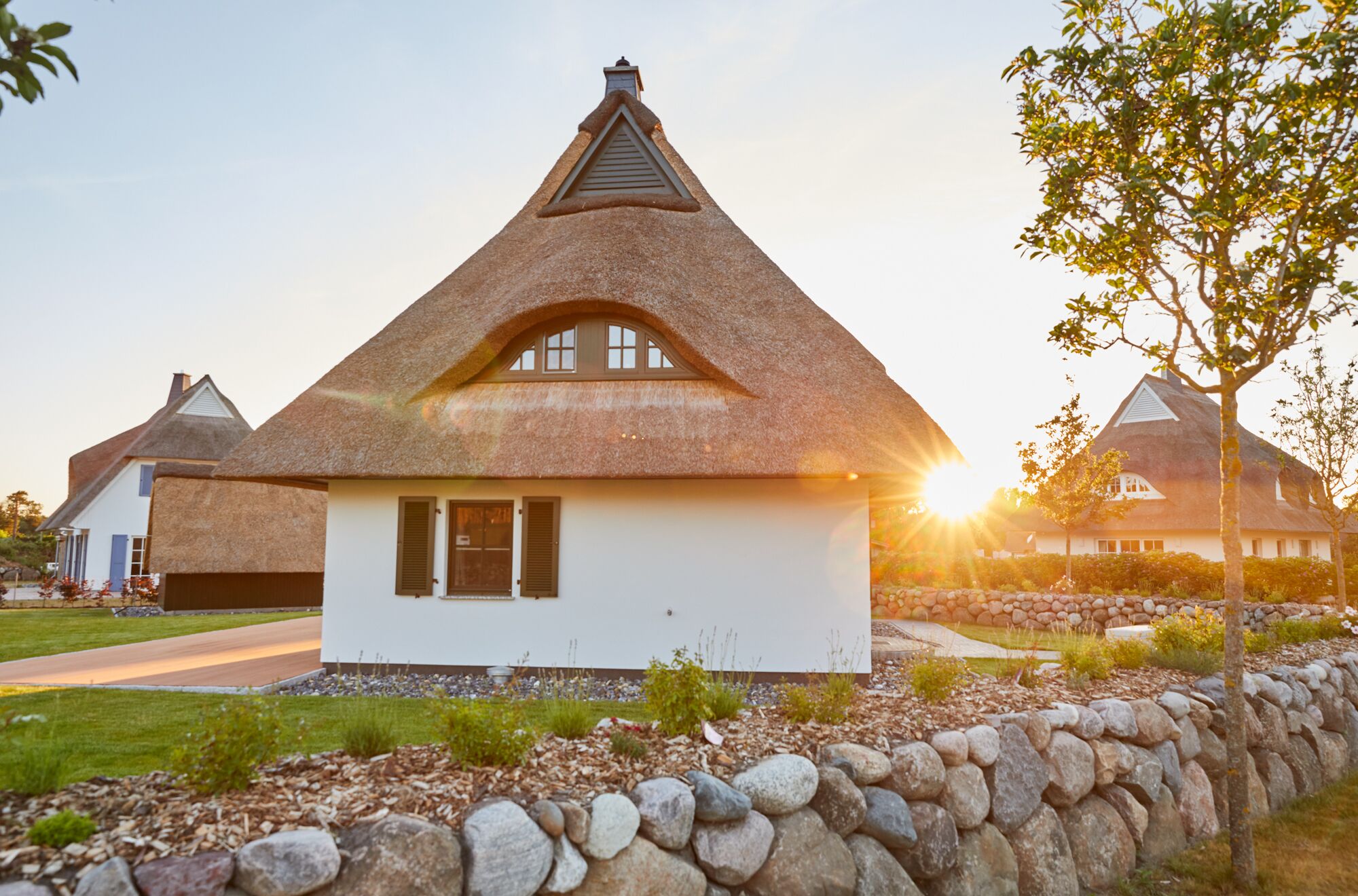A thatched-roof house with a white facade and a stone wall in front.