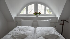 A bedroom with a skylight, a bed with white linens, and a vase with flowers.