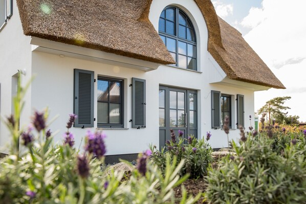 Une maison à deux étages, avec un toit de chaume, des murs extérieurs blancs et des volets noirs.