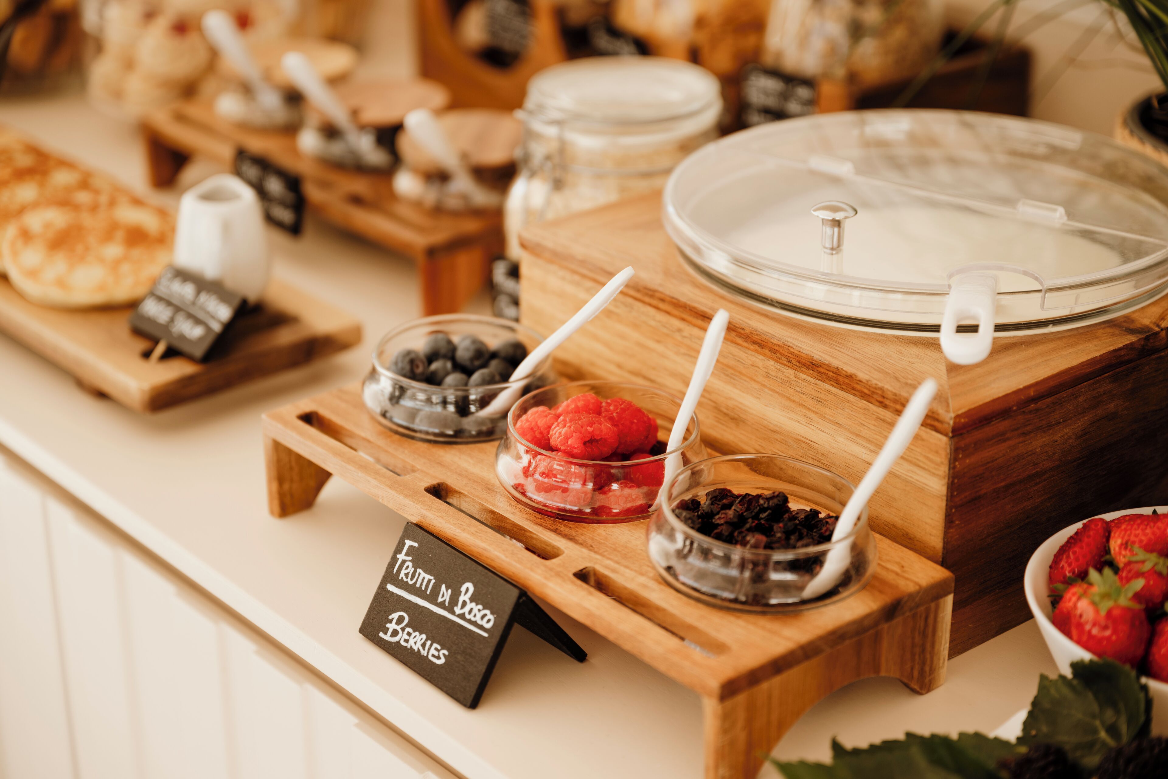 A breakfast buffet with various fruits and berries displayed on wooden stands.