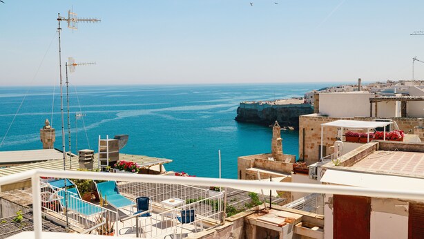 A coastal view with a clear blue sea, a rocky outcrop, and buildings with balconies overlooking the water. - Bayit Charming Place (Polignano a Mare)