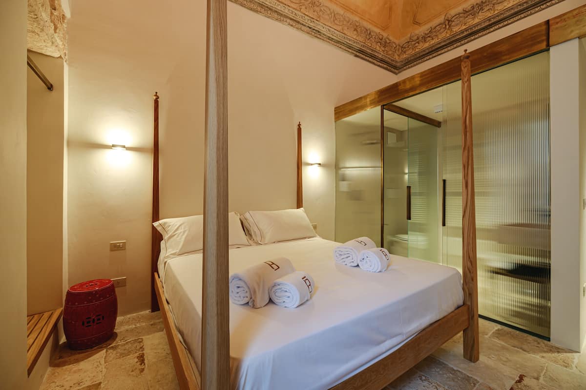 A hotel room with a four-poster bed, a glass door leading to a balcony, and a red barrel.