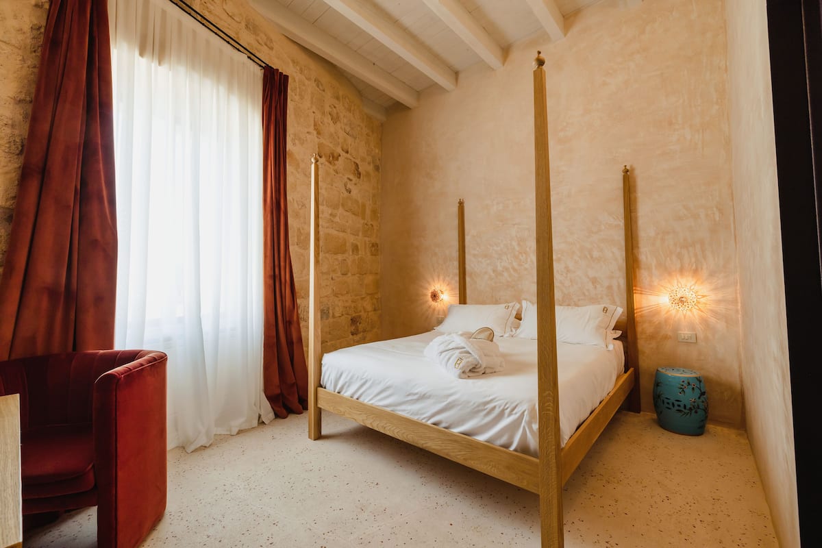 A four-poster bed in a room with stone walls and a wooden ceiling.