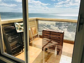 Un balcon avec vue sur la mer, un banc en bois et un porte-serviettes en métal.