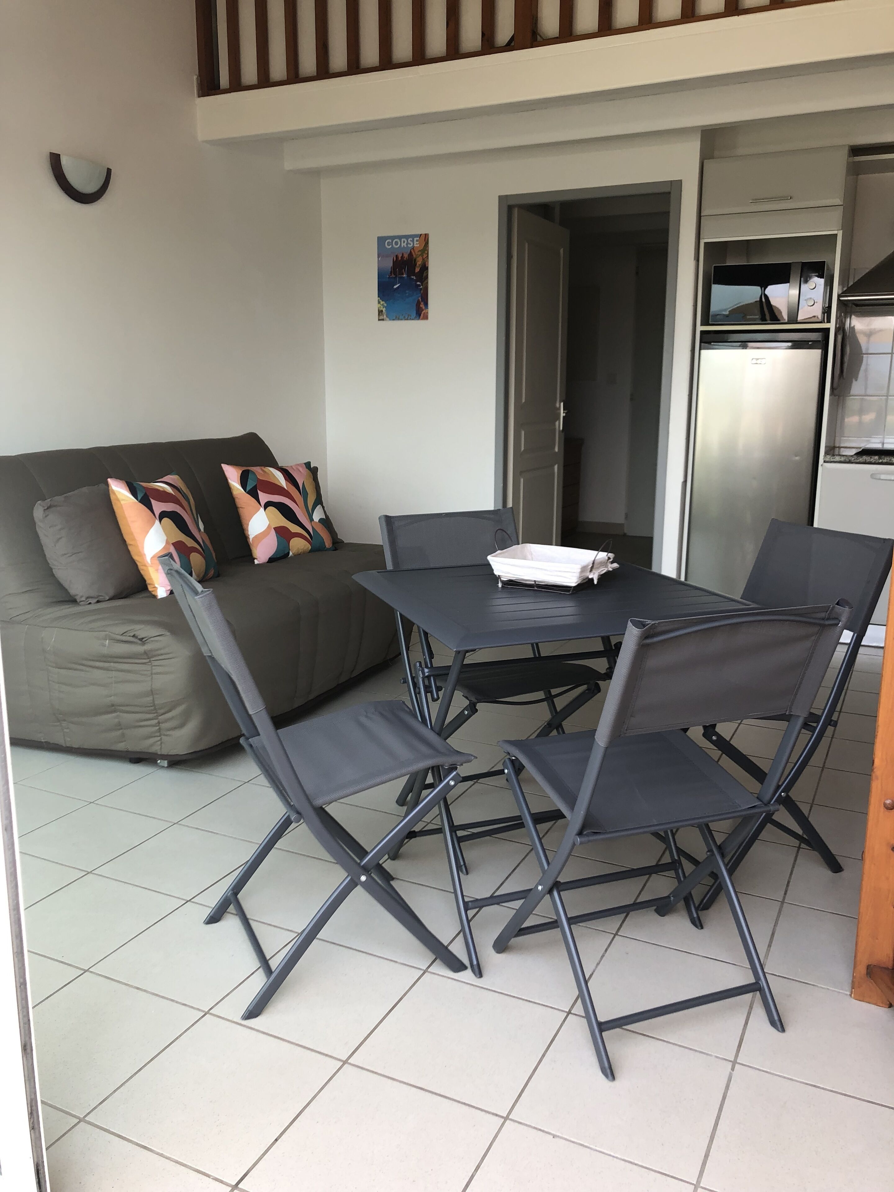 Ein gemütlicher Wohnraum mit einer Couch, einem Esstisch mit Stühlen, einem Kühlschrank und einem Bild an der Wand.