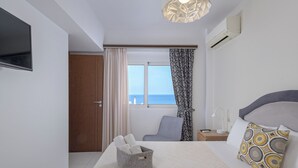 Habitación de hotel con cama, mesita de noche con lámpara, una silla, ventana con cortinas y televisión en la pared.